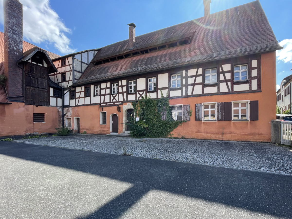Historisches Fachwerkhaus in orange-braunen T&ouml;nen mit schwarzen Holzbalken, situated on a cobblestone street with a clear blue sky in the background.