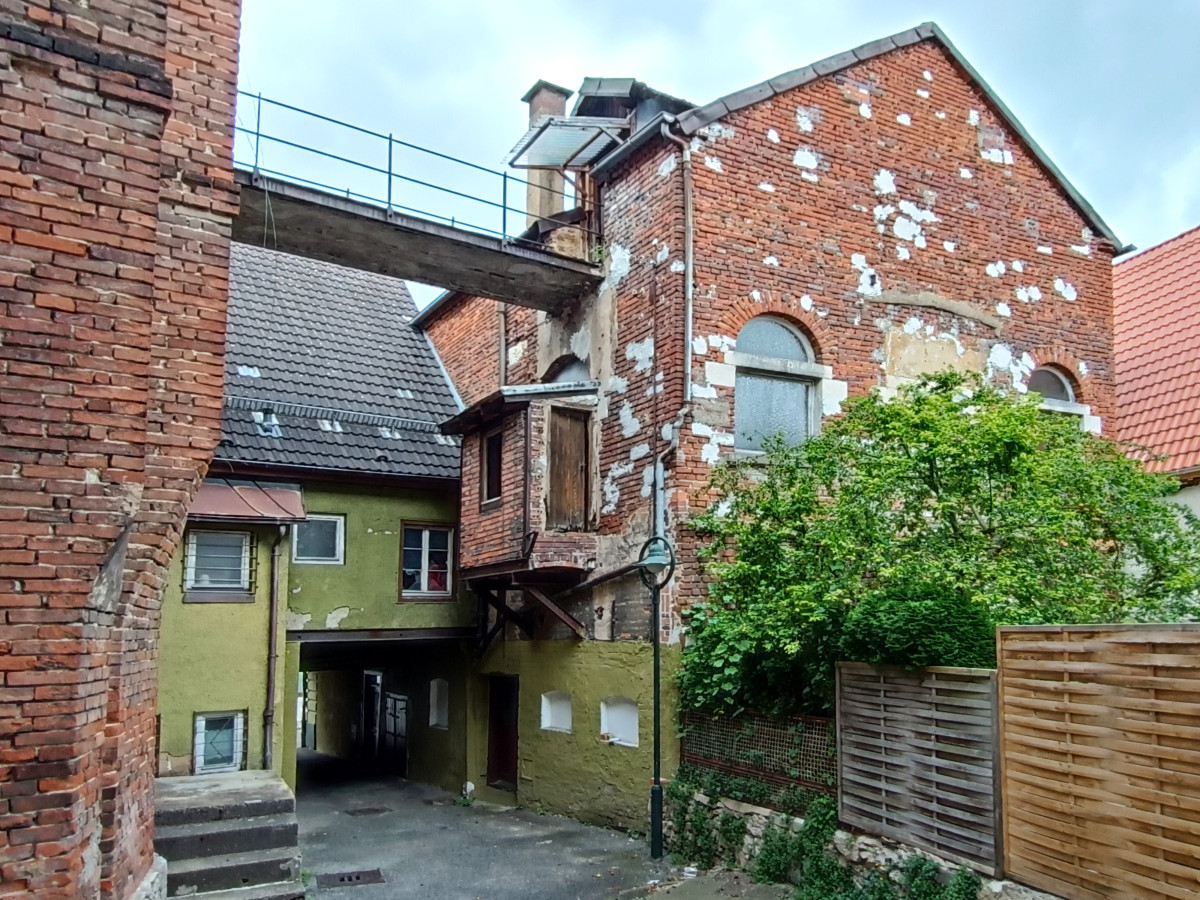 Altst&auml;dtische Backsteingeb&auml;ude mit verbundenen Anbauten und Treppe, gr&uuml;ne Fassade und Holzzaun im Vordergrund. Architektonisch interessante Mischung aus verschiedenen Geb&auml;udeteilen mit unterschiedlichen Materialien und Baustilen.