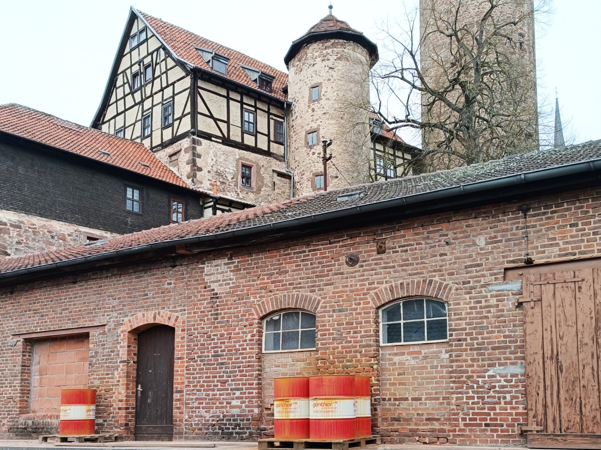 Backsteingeb&auml;ude mit Fachwerk-Turm und historischem Gem&auml;uer. Rote Bauz&auml;une markieren den Vordergrund, umgeben von Ziegelmauern und einem charakteristischen Fachwerkhaus im Hintergrund.