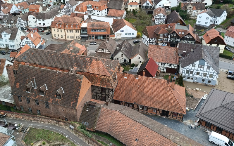 Luftaufnahme des Hahnekiez-Viertels mit dicht aneinander gebauten Fachwerkhäusern in verschiedenen Rottönen und Grautönen. Die historische Architektur zeigt eine typische mittelalterliche Stadtlandschaft mit verschachtelten Dächern und engen Gassen.