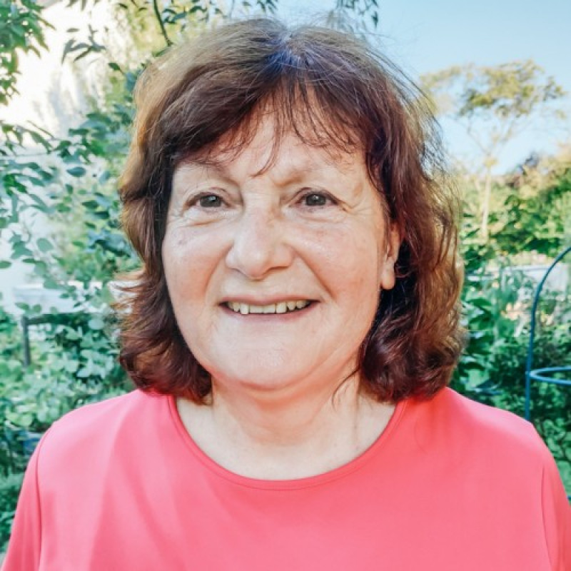 L&auml;chelnde Frau mit schulterlangen braunen Haaren und Pony, gekleidet in ein korallenfarbenes T-Shirt.